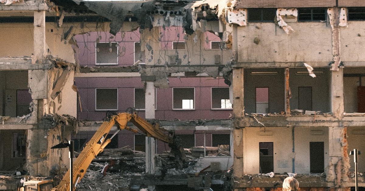 A homeowner watches on as an excavator demolishes a building to clear the site